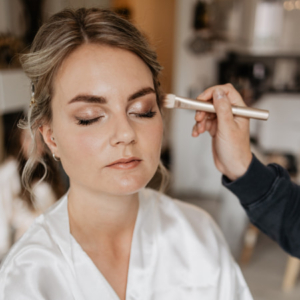 Blonde Braut wird von Hand mit Pinsel geschminkt