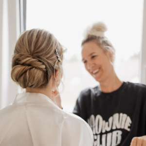 Make-up Artistin macht Haare und Make-up bei blonder Braut. Die Braut sieht man von hinten